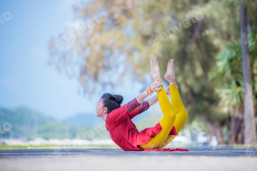 Preview: Asian young healthy woman posing practice bird of paradise yoga on stone beach with blue cloud sky a
