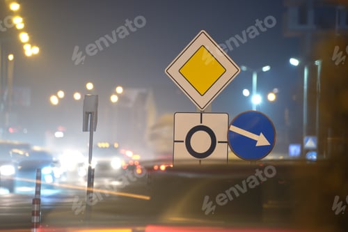 Preview: Roundabout road signs with blurred cars on city street traffic at night.