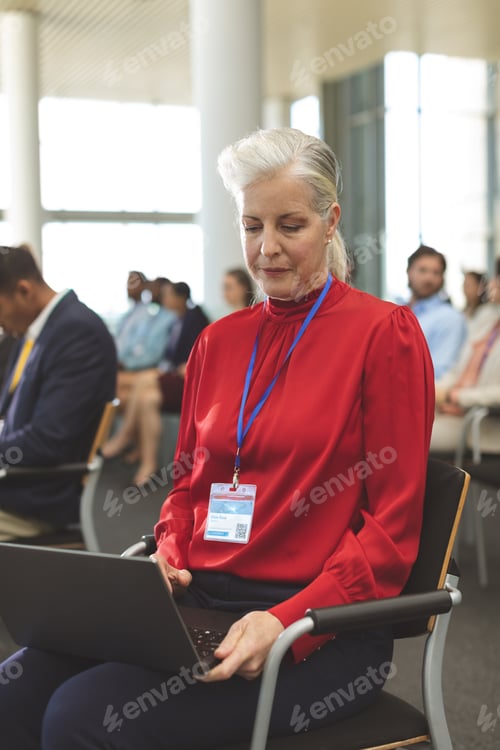 Preview: Front view of mature Caucasian businesswoman using laptop during seminar in office building