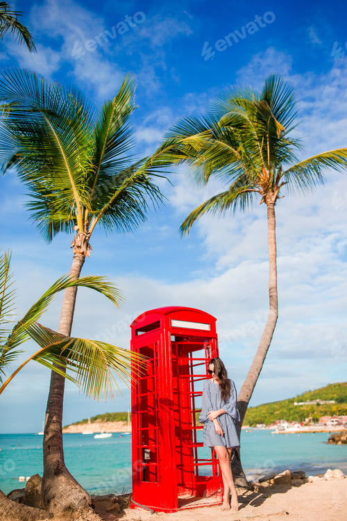 Preview: Beautiftul woman near red phone booth in Dickenson's bay Antigua. Beautiful landscape with a