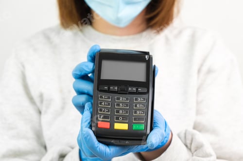 Preview: Woman in rubber gloves and face mask holding a POS terminal for payment during pandemic of