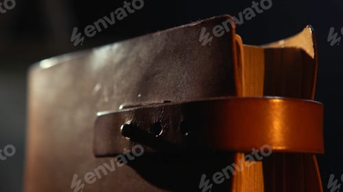 Preview: Close-up of old leather bound book with the leather straps in the dark room. Stock footage. Vintage