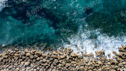 Preview: Aerial view from flying drone of crystal blue ocean water splashing on sea rocks