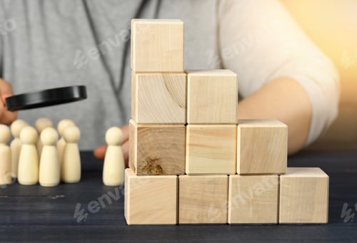 Preview: Ladder of wooden cubes on a steel, behind a man under a magnifying glass