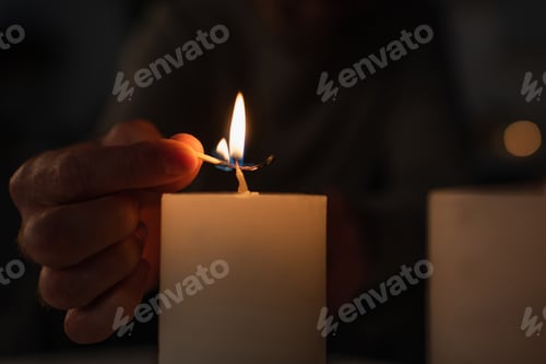 Preview: cropped view of man with burning match lighting candle on black background