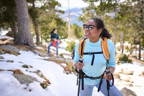 Preview: Hiker walking in snowy mountain forest trail with backpack and trekking poles