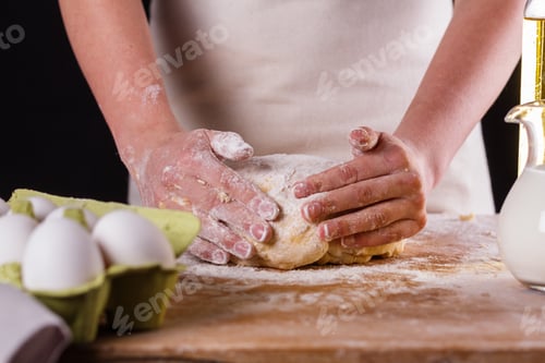 Preview: young woman in apron kneading dough on board