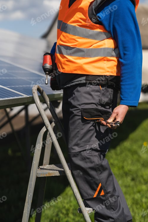 Preview: Male engineer who installs and maintains solar panels stands on a stepladder and takes out a wrench