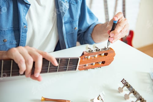 Preview: Guitar Master hands placing and adjusting with a screwdriver the peg of a classical instrument.