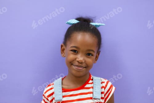 Preview: Portrait of smiling african americana elementary schoolgirl against purple background
