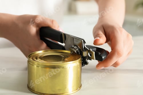 Preview: Woman opening tin with can opener at white table, closeup