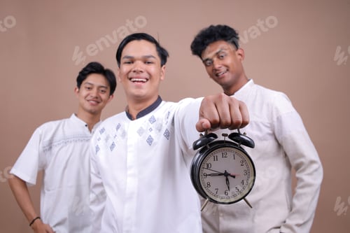 Preview: Young Asian Muslim Man Holding Alarm Clock And Standing In Front Of His Friends