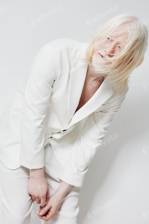 Preview: Fashion model in a white suit with long blond hair, striking a playful pose against a bright