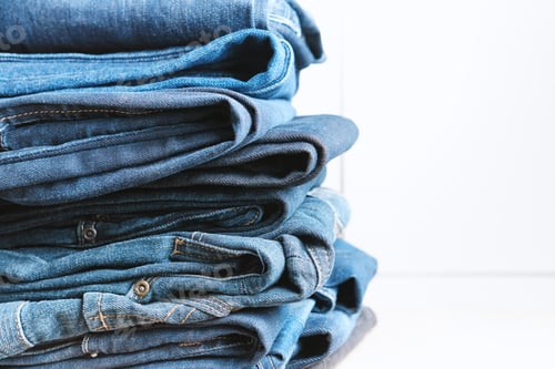 Preview: Stack of Folded Denim Jeans on White Surface