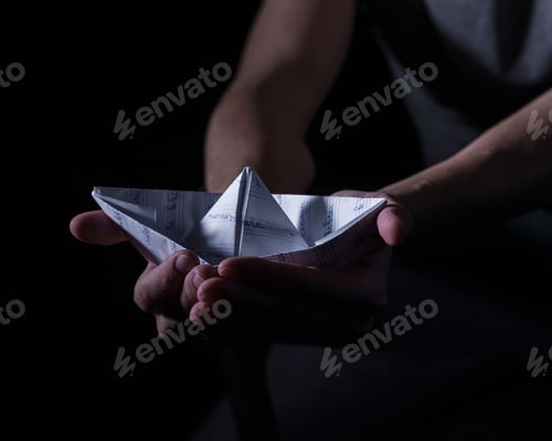 Preview: white paper boat in the hands of an adult in a dark key, psychology
