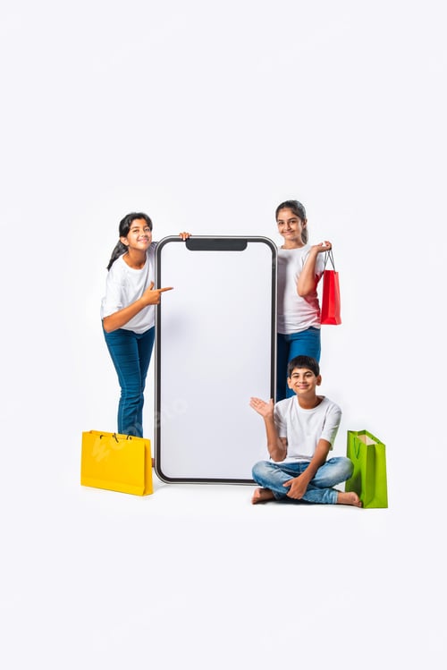 Preview: Indian kids standing with shopping bags near big tall smartphone cutout with blank screen