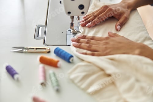 Preview: African-American seamstress sews white fabric with machine at workplace in studio