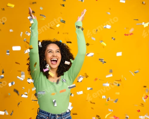 Preview: Studio Shot Of Excited Woman Celebrating Big Win Showered In Tinsel Confetti On Yellow Background