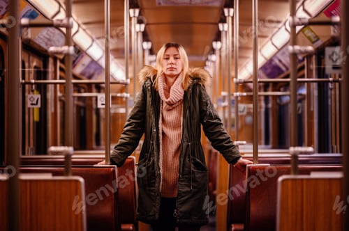 Preview: Young blonde girl in winter outfit standing in empty old metro train railway carriage with lights on