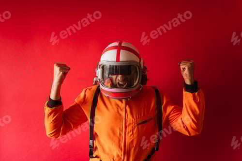 Preview: Astronaut with a helmet and an orange space suit with fists raised in sign of victory