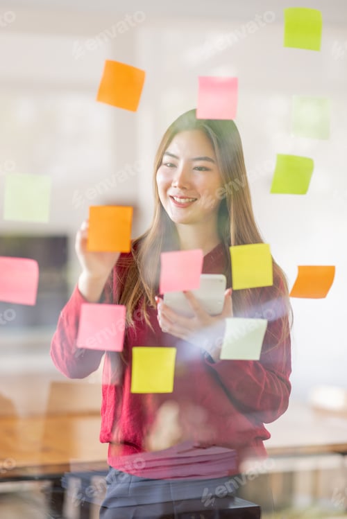 Preview: Asian businesswoman creating project plan on office wall with sticky paper notes. stylish confident