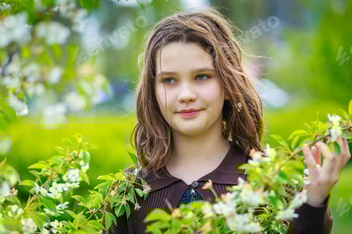 Preview: Beautiful girl among cherry flowers in spring. Portrait of a girl with brown hair and green eyes.
