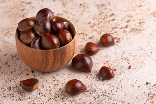 Preview: Wooden bowl filled with fresh chestnuts on beige travertine stone surface