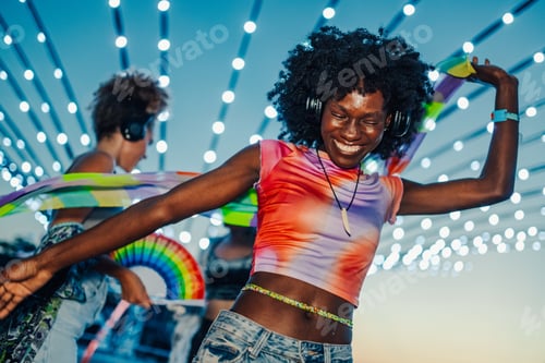 Preview: Young woman dancing with friends at music festival under string lights