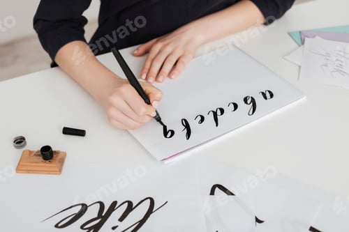 Preview: Close up photo of young woman hands writing alphabet on paper on desk isolated