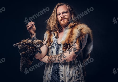 Preview: Portrait of a tattooed redhead hipster male holds a keeps the scarecrow of an owl in a studio