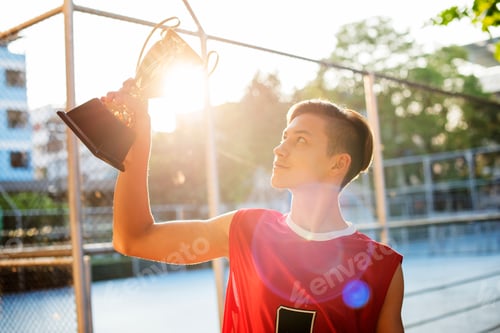 Preview: Caucasian teenage boy in sporty clothes holding up a trophy outdoors
