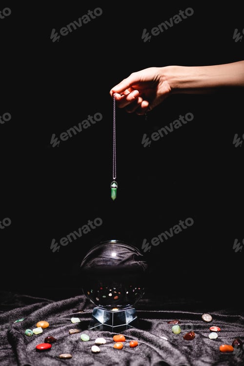 Preview: cropped view of fortuneteller holding stone above crystal ball with fortune telling stones on black