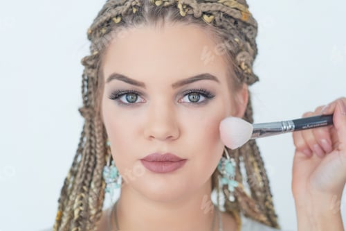 Preview: Professional makeup artist working with beautiful young woman. bright blonde model