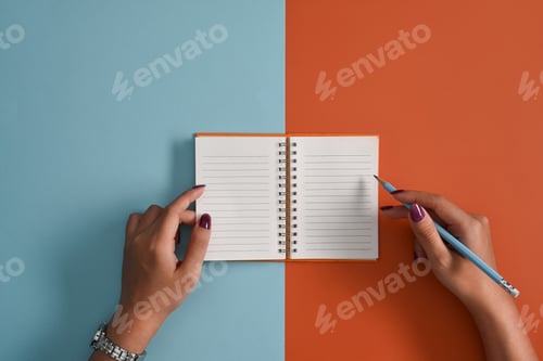 Preview: Above view woman holding pencil writing on empty notepad.