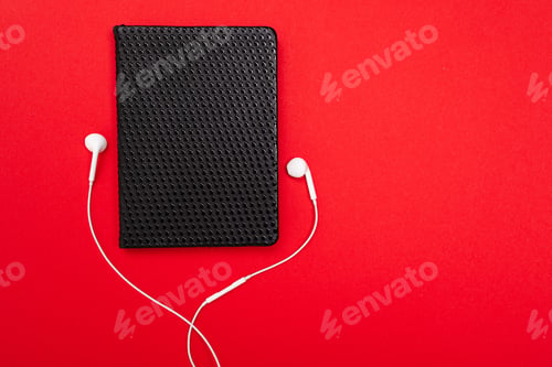 Preview: Black notebook with white earphones isolated on red background