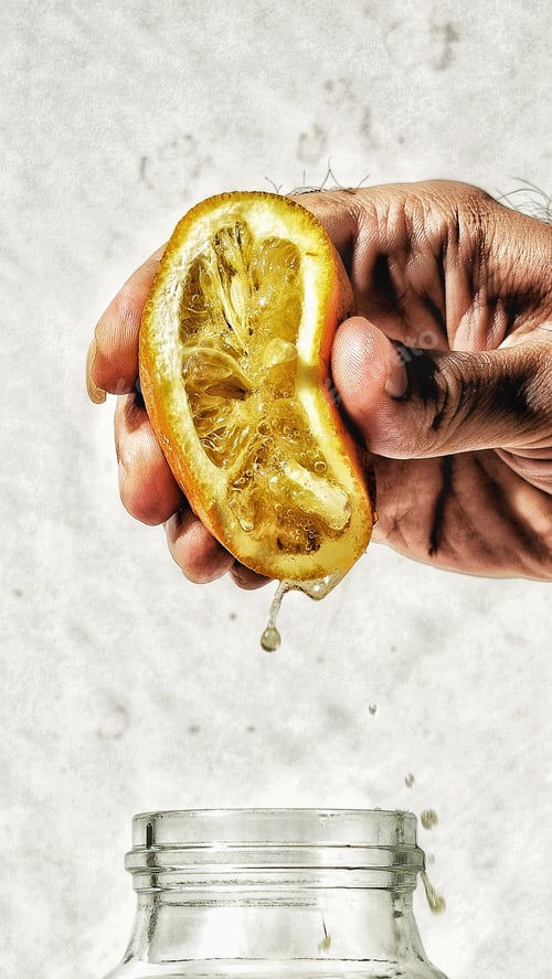 Preview: Vertical shot of a hand squeezing the lemon juice from a half-lemon into a glass bottle