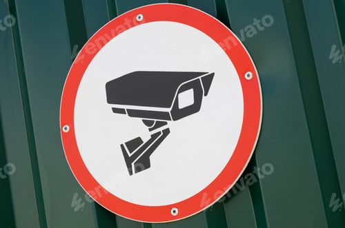 Preview: CCTV in operation sign on green corrugated fence background. White and red sign. Safety at facility.