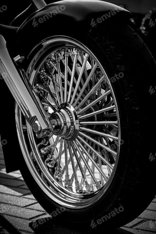 Preview: Close-up grayscale shot of a shiny motorcycle tire on a tile pavement on a sunny day