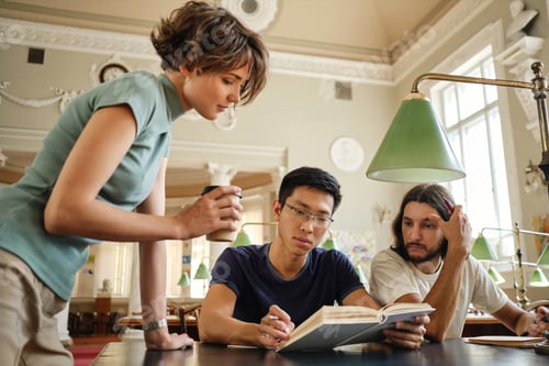 Preview: Attractive tutor helping multinational students with study during lesson in university library