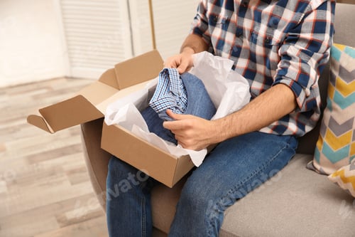 Preview: Young man opening parcel at home, closeup