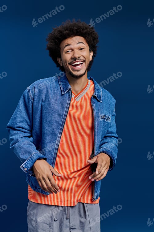 Preview: Young handsome man smiles warmly in casual outfit against a vibrant blue backdrop