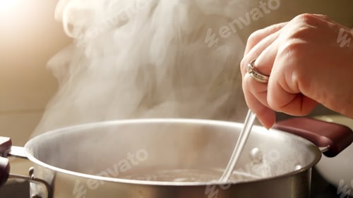 Preview: Female hand stirring boiling soup in metal pan with spoon. Vapour slowly rising from hot water.