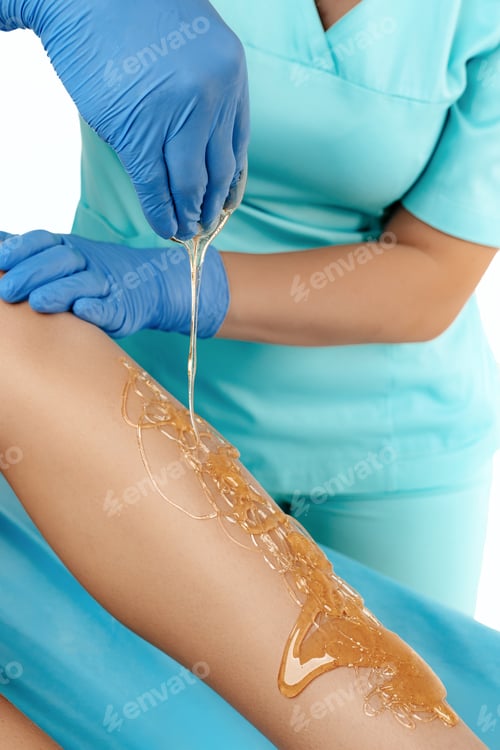 Preview: Close-up image of sugar depilation procedure for women in beauty salon over white background.
