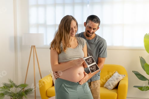 Preview: Pregnancy couple looking picture of ultrasound, smiling happily touching belly