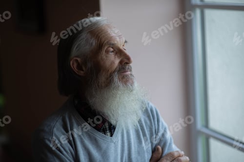 Preview: Side view of senior man with gray beard looking through window