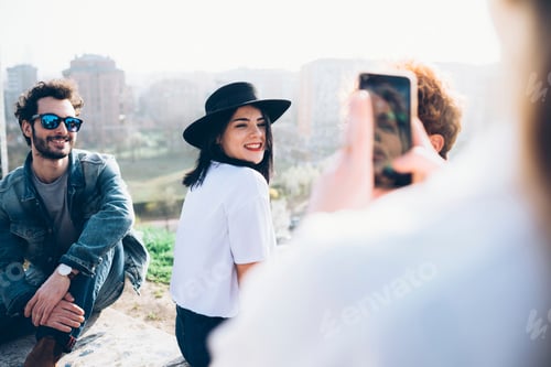 Preview: Group of friends enjoying roof party, young woman photographing friends using smartphone