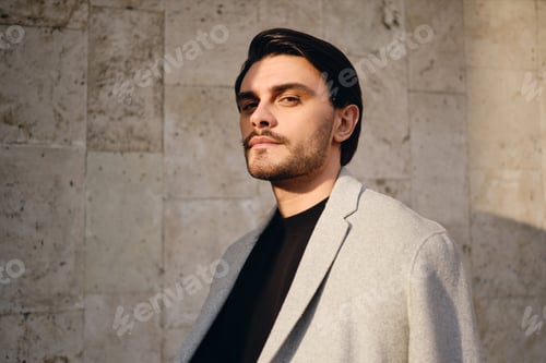 Preview: Portrait of young confident brunette man in coat intently looking in camera outdoor