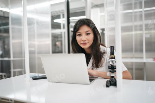 Preview: Young scientist in white lab coat working with binocular microscope in the material science lab
