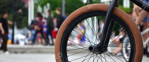 Preview: A BMX bike wheel against the backdrop of a blurred street with cycling riders. Extreme Sports