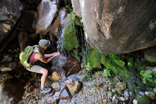 Preview: High angle view of hiker cupping hands under waterfall collecting water